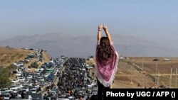 An unveiled woman stands on top of a vehicle as thousands make their way towards the cemetery in Saghez, Mahsa Amini's hometown in Kurdistan Province, to mark 40 days since her death in late October.