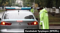 Қызмет көлігінің қасында тұрған полиция қызметкері. Көрнекі сурет.