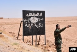 A Syrian soldier takes a selfie with an Islamic State (IS) group billboard at the Ithraya-Rasafa highway near the city of Raqqa on July 9, 2017.