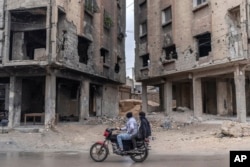 People ride past buildings damaged by air strikes during the Assad rule in Douma, on the outskirts of Damascus, in December.